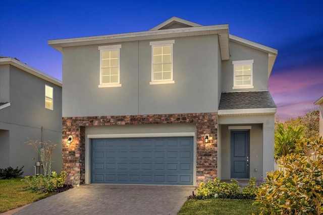 traditional-style house featuring an attached garage, stucco siding, stone siding, and driveway