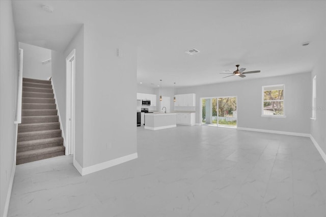 unfurnished living room with baseboards, marble finish floor, visible vents, ceiling fan, and stairway