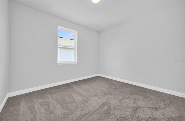 spare room with baseboards and dark colored carpet