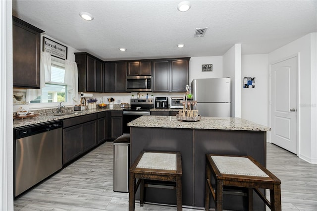 5424 Companion Ln, Tampa, FL 33619 - kitchen with appliances with stainless steel finishes, a breakfast bar, a center island, light stone counters, and dark brown cabinets