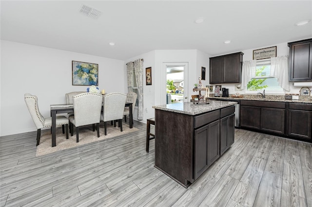 5424 Companion Ln, Tampa, FL 33619 - kitchen featuring light wood finished floors, dark brown cabinets, a center island, light stone counters, and recessed lighting