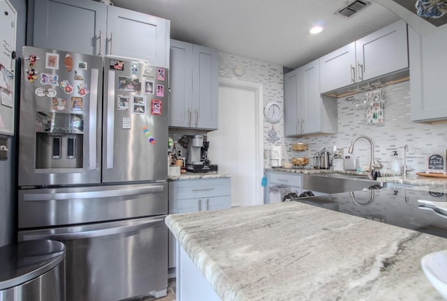 kitchen with light stone counters, visible vents, a sink, stainless steel fridge with ice dispenser, and tasteful backsplash