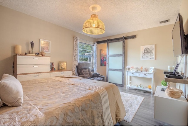 bedroom featuring a textured ceiling, a barn door, visible vents, and wood finished floors