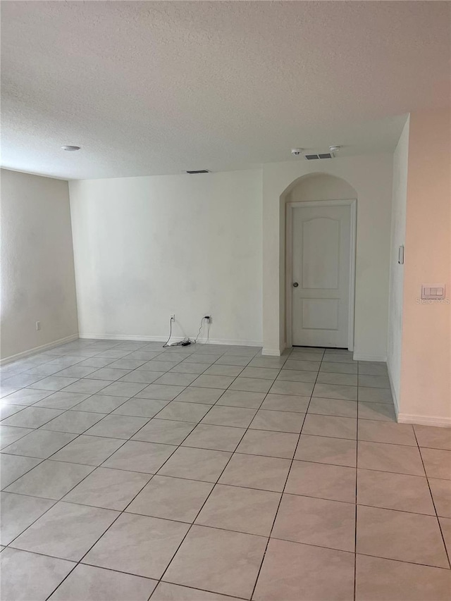 spare room featuring light tile patterned floors, a textured ceiling, and arched walkways