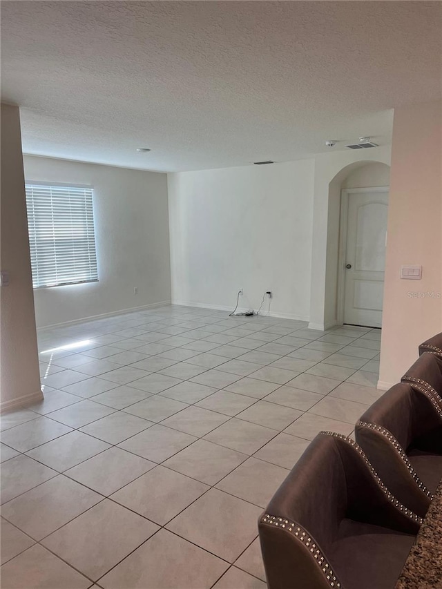 living area with arched walkways, light tile patterned floors, a textured ceiling, and baseboards