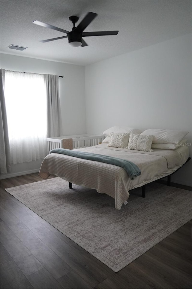 bedroom with a textured ceiling, visible vents, wood finished floors, and a ceiling fan