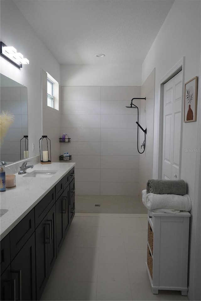 bathroom with tiled shower, tile patterned floors, double vanity, and a sink