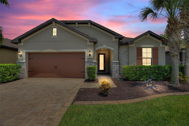 view of front of home featuring stucco siding, stone siding, decorative driveway, and a garage