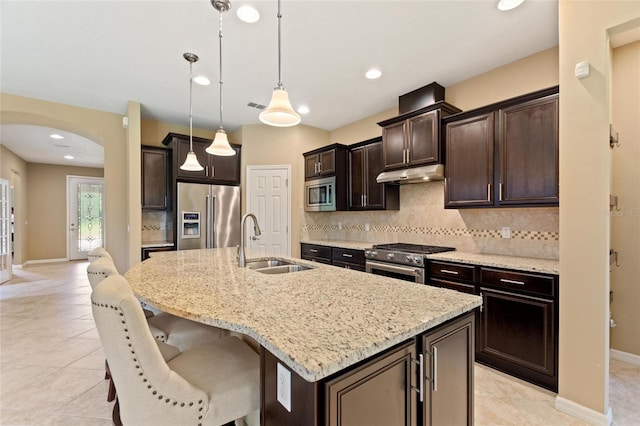 kitchen with appliances with stainless steel finishes, a sink, under cabinet range hood, arched walkways, and backsplash