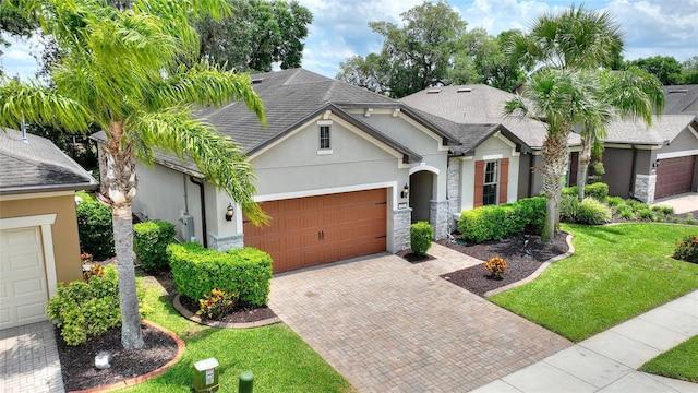 view of front of house with stucco siding, a garage, decorative driveway, a front yard, and roof with shingles