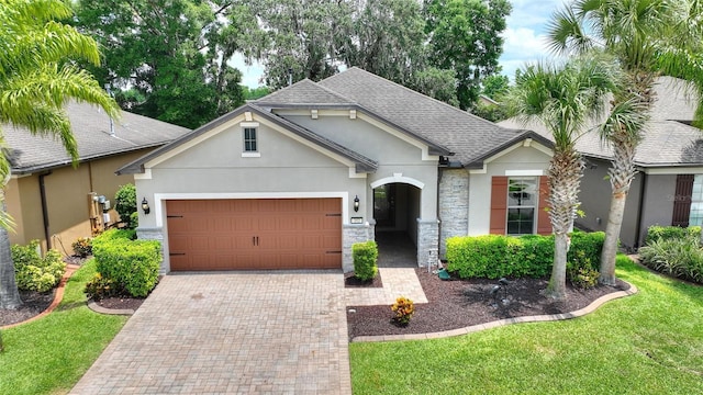 ranch-style house with stucco siding, an attached garage, decorative driveway, roof with shingles, and stone siding