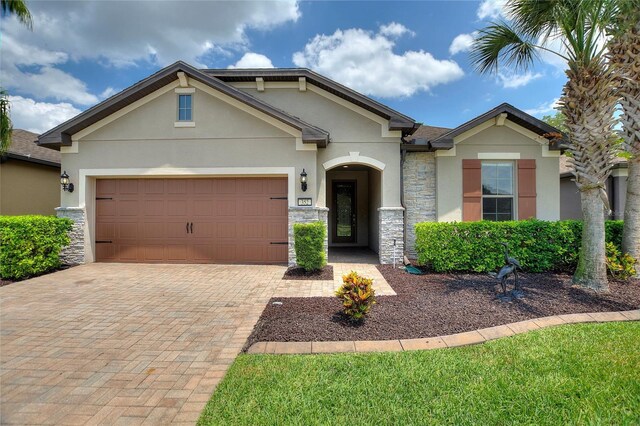 craftsman house featuring stucco siding, stone siding, decorative driveway, and a garage