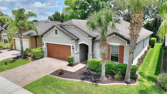 view of front of property featuring stucco siding, a garage, stone siding, decorative driveway, and a front lawn
