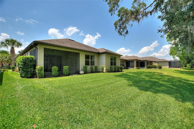 back of property featuring a lawn, stucco siding, a sunroom, and ceiling fan