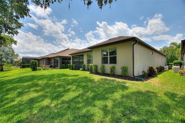 back of property with stucco siding, a yard, and central AC unit