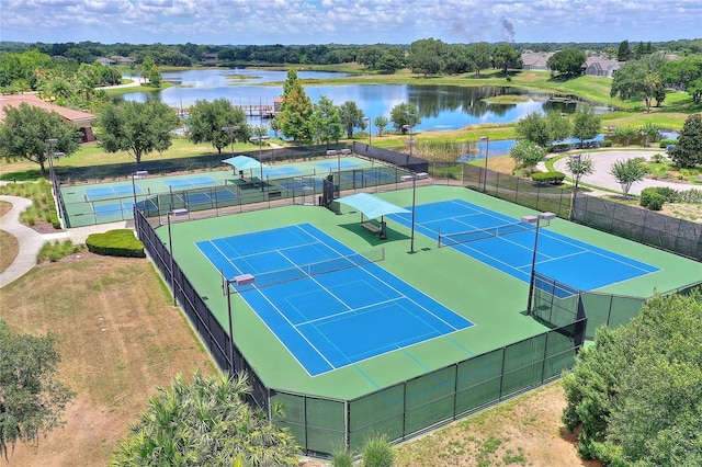 view of tennis court featuring a water view, fence, and view of wooded area