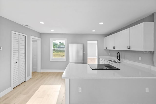 4445 Stuart Ave, Titusville, FL 32780 - kitchen featuring refrigerator, black electric stovetop, a sink, white cabinetry, and recessed lighting