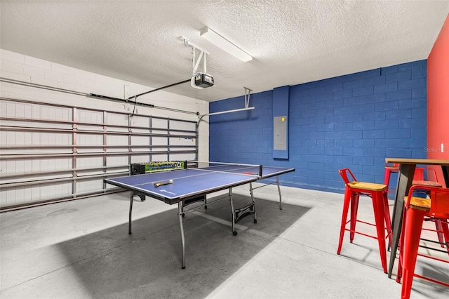 game room featuring a garage, concrete flooring, electric panel, a textured ceiling, and concrete block wall