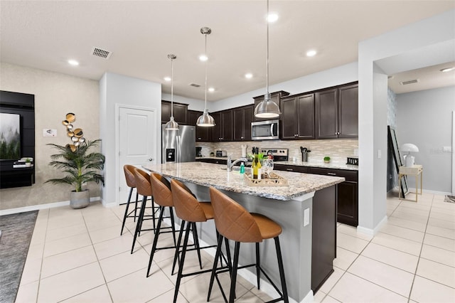 kitchen with stainless steel appliances, light tile patterned floors, backsplash, a breakfast bar area, and a sink
