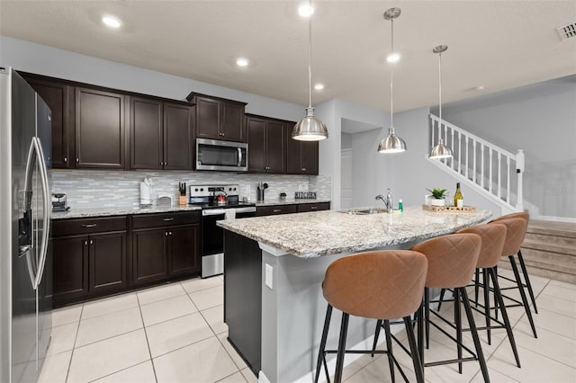 kitchen featuring stainless steel appliances, tasteful backsplash, a kitchen breakfast bar, light stone countertops, and a center island with sink