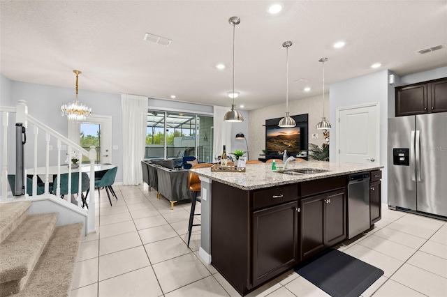 kitchen with appliances with stainless steel finishes, a sink, open floor plan, light stone counters, and dark brown cabinetry
