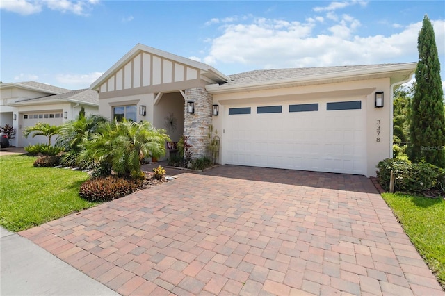 view of front facade featuring stucco siding, decorative driveway, an attached garage, a front yard, and stone siding