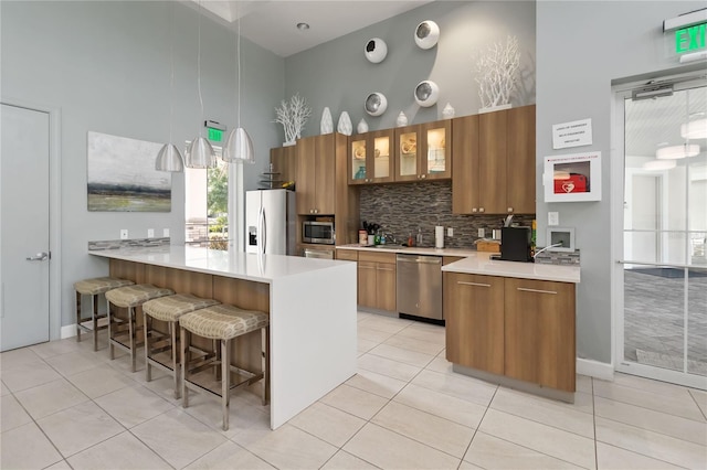 3378 Sagebrush St, Harmony, FL 34773 - kitchen featuring appliances with stainless steel finishes, a towering ceiling, brown cabinetry, a kitchen breakfast bar, and a peninsula
