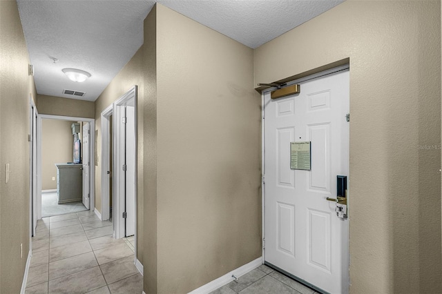 foyer entrance with light tile patterned floors, a textured ceiling, and baseboards