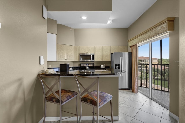 kitchen featuring appliances with stainless steel finishes, dark countertops, a peninsula, a kitchen breakfast bar, and light tile patterned floors