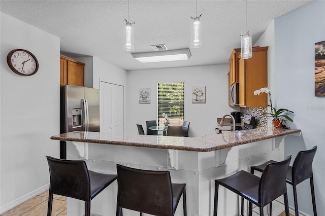 kitchen featuring stainless steel appliances, brown cabinets, a breakfast bar area, stone counters, and a textured ceiling