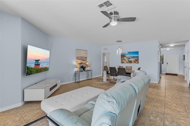 living room with ceiling fan, baseboards, a textured ceiling, light tile patterned floors, and a chandelier
