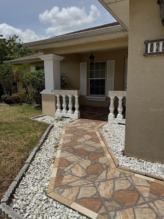 829 Anza Ave, Lehigh Acres, FL 33971 - view of exterior entry featuring covered porch, stucco siding, and a yard