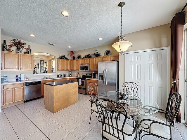 219 Rosso Dr, Davenport, FL 33837 - kitchen featuring stainless steel appliances, arched walkways, a kitchen island, a textured ceiling, and light tile patterned flooring