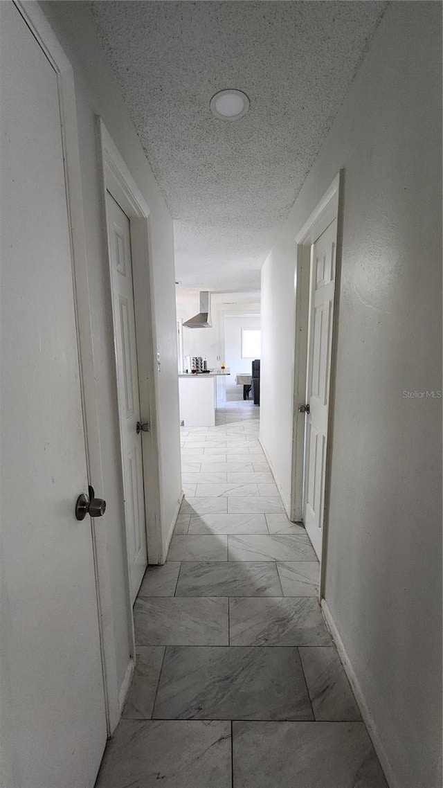 hall with marble finish flooring, a textured ceiling, and baseboards