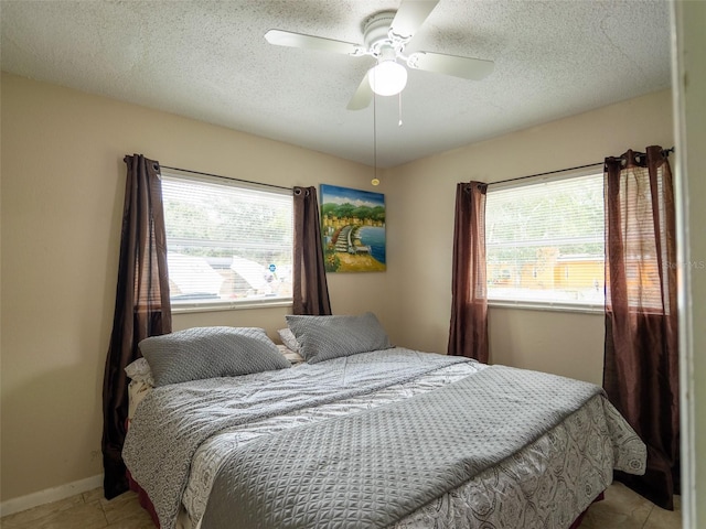 bedroom featuring multiple windows, a textured ceiling, tile patterned floors, and a ceiling fan