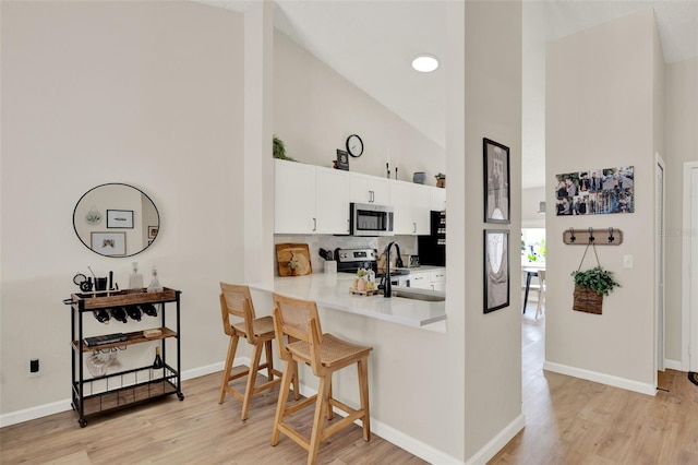 1050 Dees Dr, Oviedo, FL 32765 - kitchen with appliances with stainless steel finishes, high vaulted ceiling, a breakfast bar, light wood finished floors, and white cabinetry