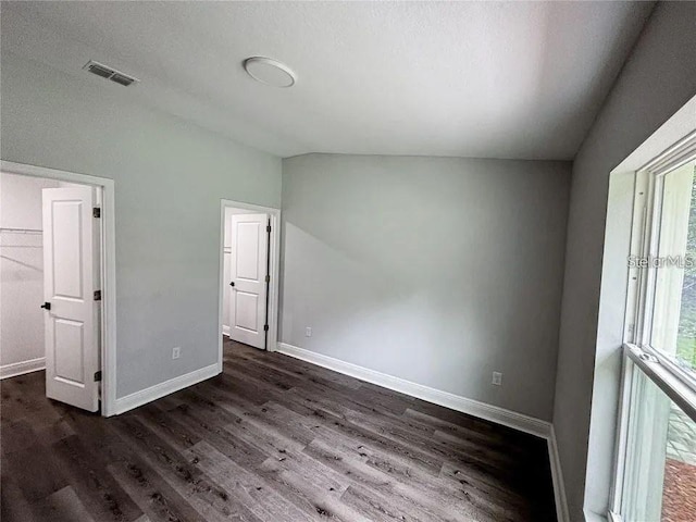 unfurnished bedroom featuring multiple windows, dark wood-style floors, baseboards, and vaulted ceiling