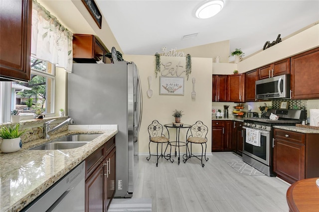 906 Elm Forest Dr, Minneola, FL 34715 - kitchen featuring appliances with stainless steel finishes, vaulted ceiling, a sink, light stone countertops, and light wood finished floors