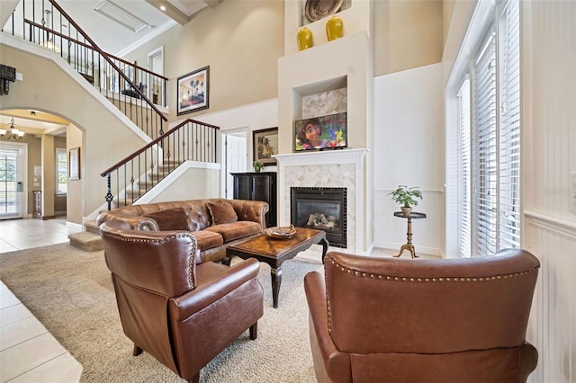 7550 Gathering Dr, Reunion, FL 34747 - tiled living room featuring stairway, arched walkways, a towering ceiling, a tiled fireplace, and a chandelier