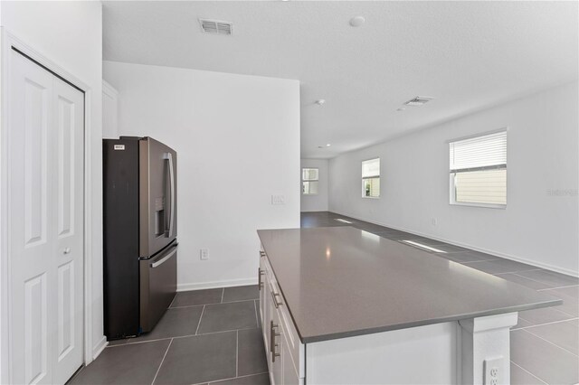 7728 Stone Creek Trl, Kissimmee, FL 34747 - kitchen with stainless steel fridge, dark countertops, a kitchen island, white cabinetry, and dark tile patterned floors