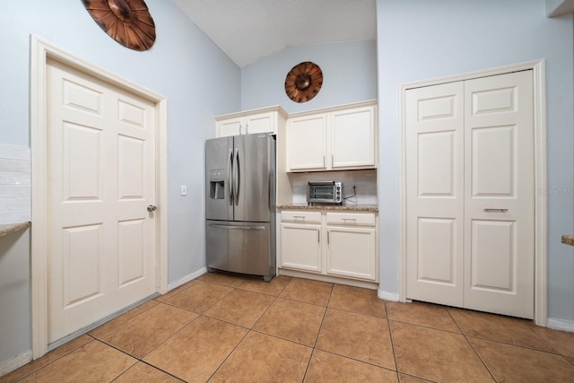 402 Ohio Way, Kissimmee, FL 34759 - kitchen with stainless steel fridge with ice dispenser, vaulted ceiling, light tile patterned floors, white cabinets, and baseboards