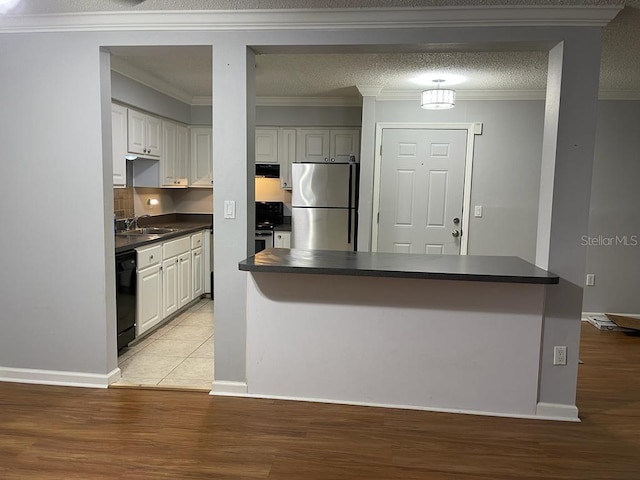 kitchen with stainless steel appliances, dark countertops, a sink, crown molding, and light wood finished floors