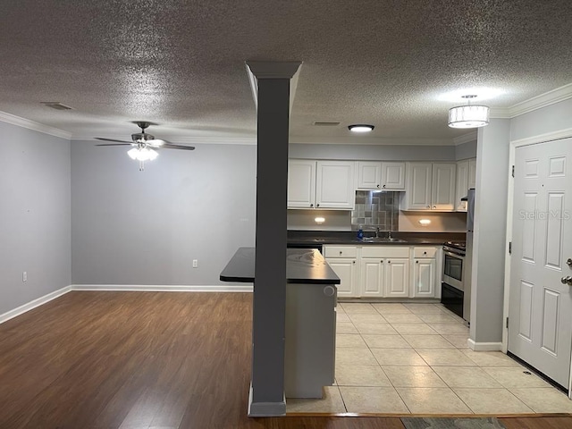 kitchen with a sink, dark countertops, crown molding, white cabinets, and stainless steel range oven