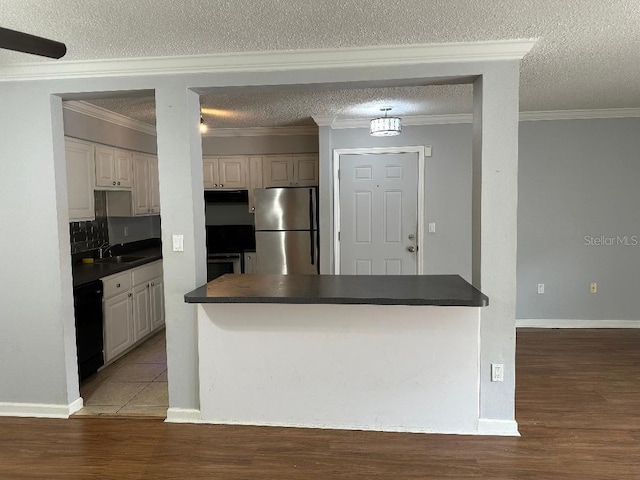 kitchen with appliances with stainless steel finishes, dark countertops, under cabinet range hood, crown molding, and light wood finished floors
