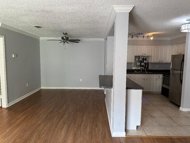 kitchen with freestanding refrigerator, ceiling fan, dark countertops, a sink, and white cabinets