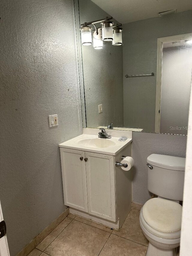 half bathroom featuring tile patterned floors, toilet, vanity, baseboards, and a textured wall