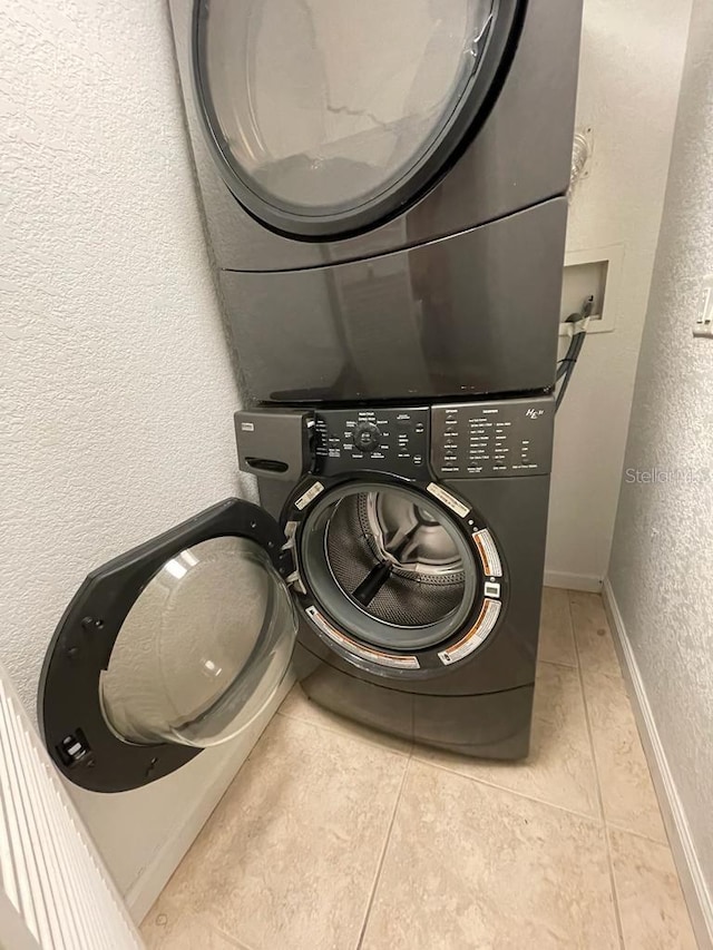 washroom with stacked washer / drying machine, a textured wall, light tile patterned flooring, and baseboards
