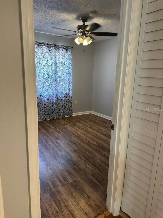 spare room with a ceiling fan, a textured ceiling, dark wood-type flooring, baseboards, and a smoke detector