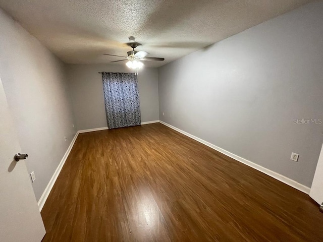 empty room with a ceiling fan, dark wood-type flooring, a textured ceiling, and baseboards