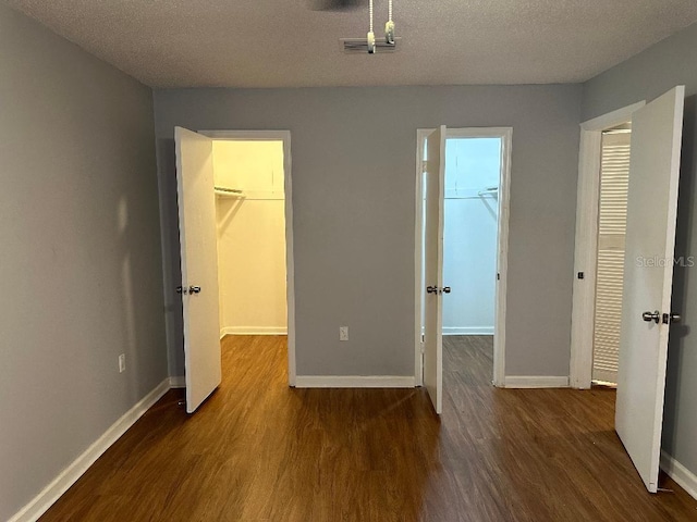 unfurnished bedroom with a walk in closet, wood finished floors, a closet, baseboards, and a textured ceiling